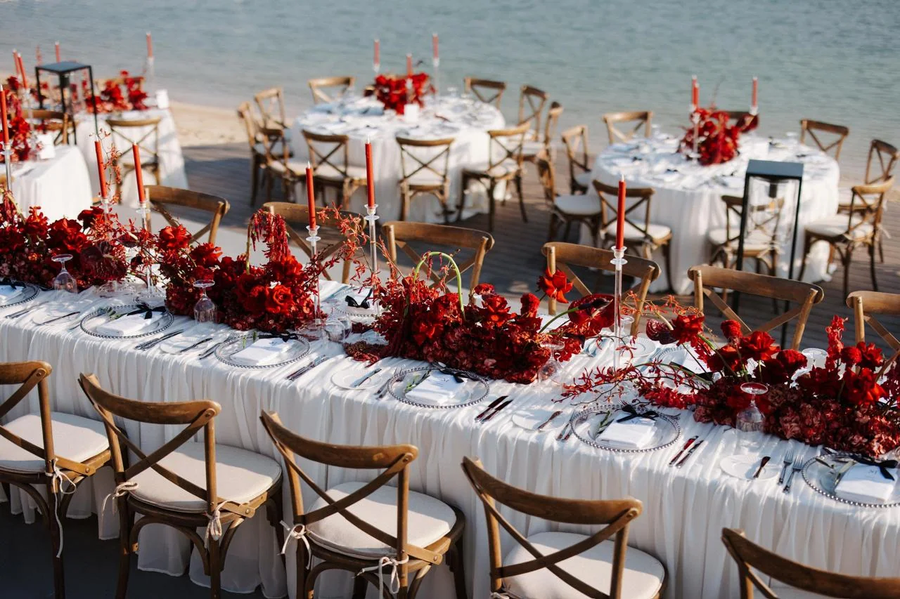 Elegant waterfront event tables with red floral arrangements